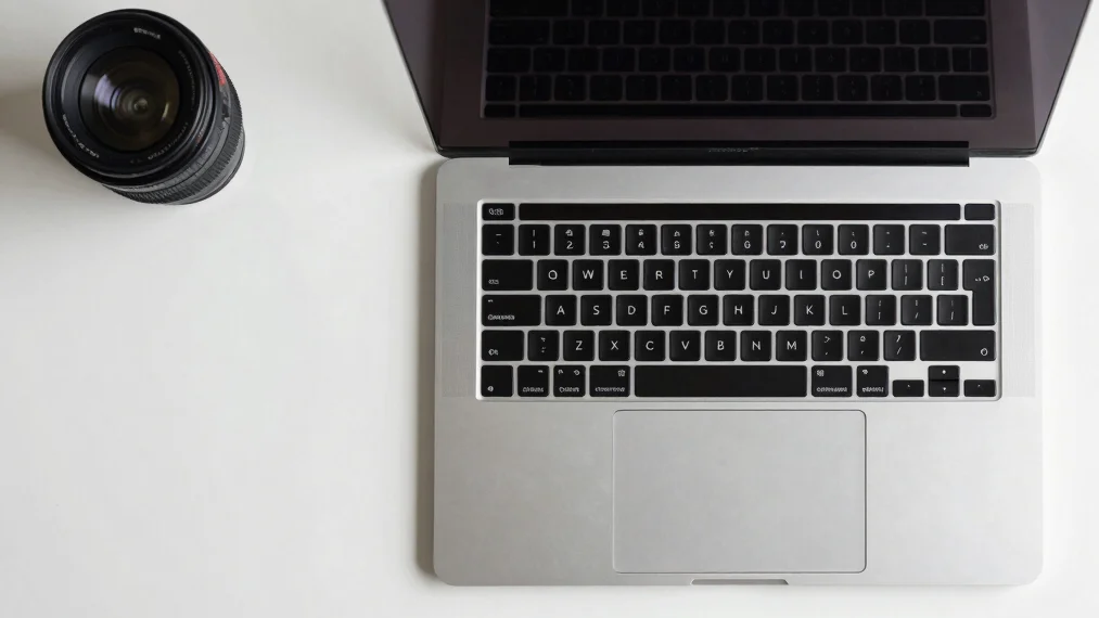 Overhead flat-lay of a sleek silver laptop on a minimalist desk, bright studio light, clean editorial product photograph